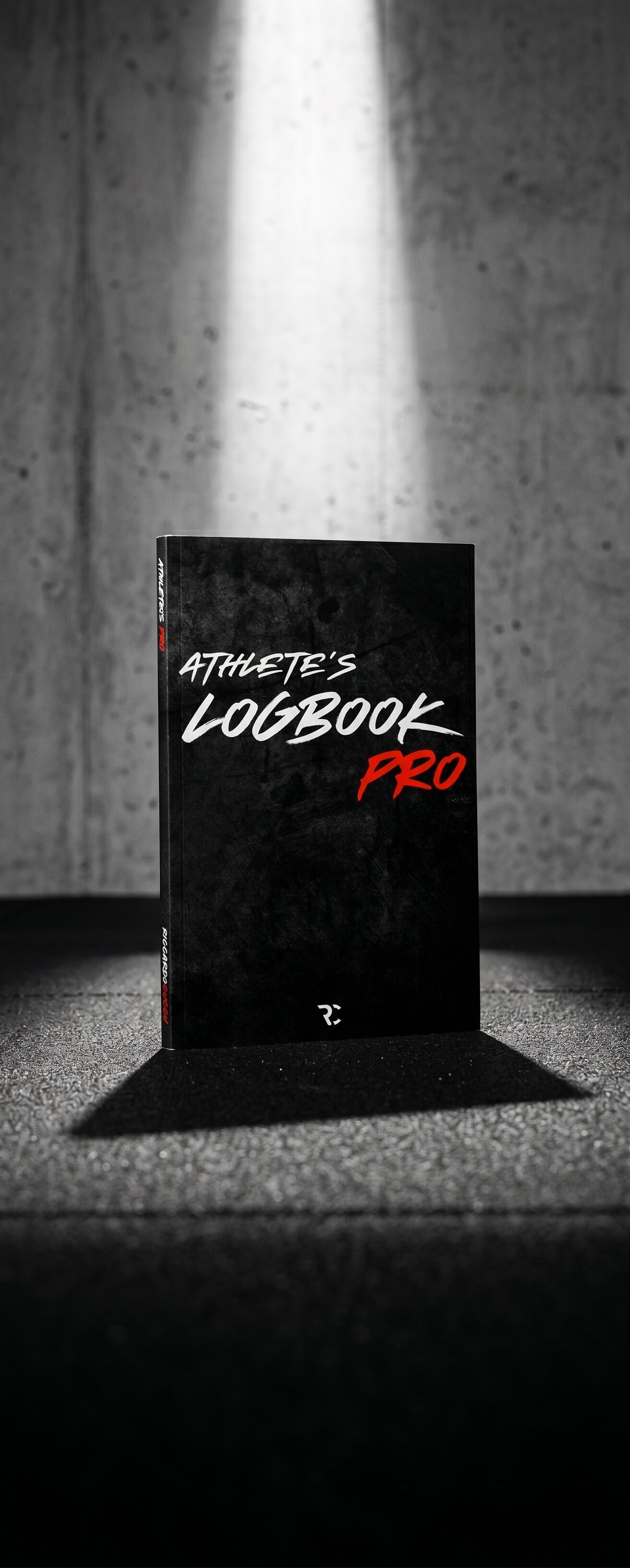 Logbook PRO, diario di allenamento, copertina morbida nera con wordmark rosso, su tavolo in legno scuro con disco 2.5kg e penna